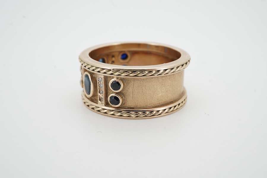 A sapphire and diamond ring, the wide band set to the front with oval and circular-cut sapphires spaced by lines of single-cut diamonds, between rope-twist borders, size V1/2, no assay marks, gross weight 12 grams, Condi
